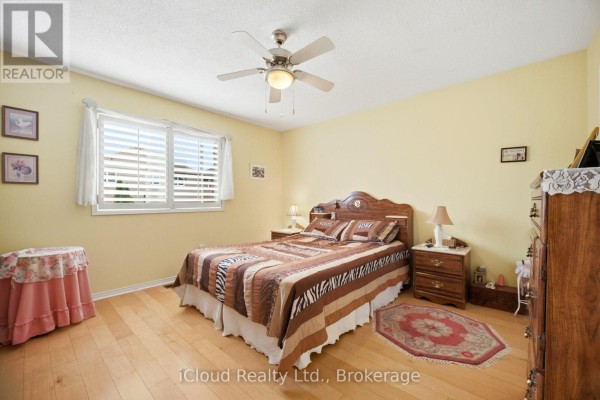 Bedroom with a wooden bed, patterned comforter, and hardwood floors - 6332 Glen Meadows Road Mississauga
