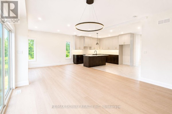 Open-concept living area and kitchen with light wood floors, white walls, and large windows. - 6333 Jewel Common, Niagara Falls