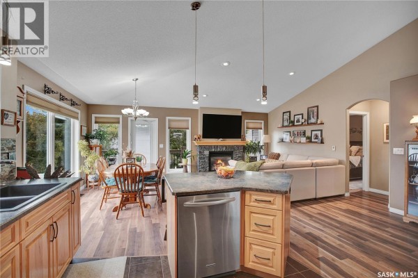 Kitchen island with a dishwasher overlooks a dining area, living room with a fireplace, and a hallway. - 634 Allwood Manor, Saskatoon