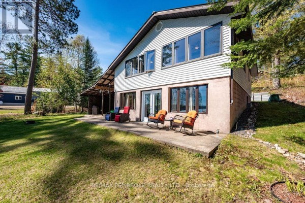 Rear exterior of a light-colored house with a concrete patio, outdoor chairs, and large windows. - 634 Goldfinch Way, Head, Clara And Maria