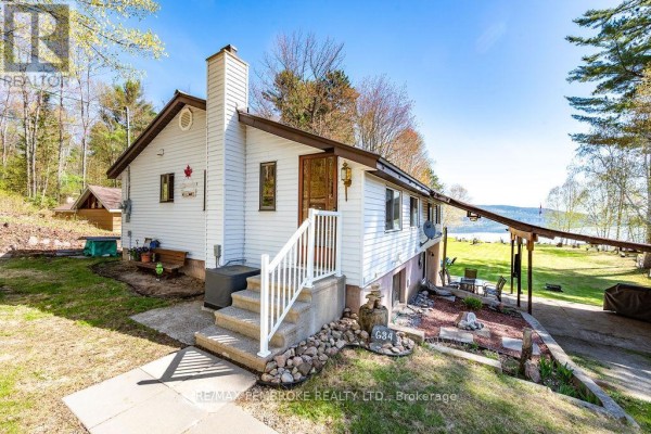 Front view of a white house with a stone chimney, stairs, and a lake view. - 634 Goldfinch Way, Head, Clara And Maria