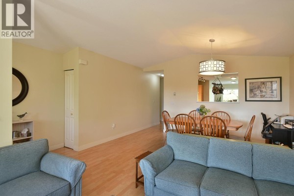 View of the open-concept living and dining area from the sofa, showing light wood floors and beige walls. - 6340 Williams Place, Sechelt