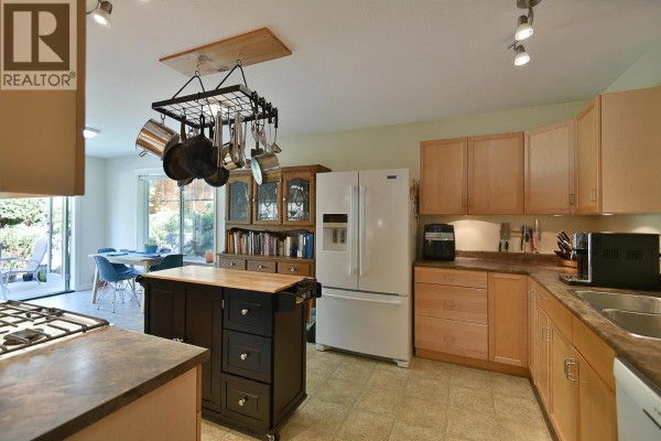 Kitchen with wood cabinets, island on wheels, white refrigerator, and view of a breakfast nook. - 6340 Williams Place, Sechelt