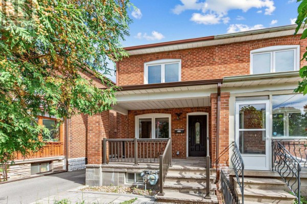 Close-up of the red brick facade of a row house, showing the porch with railings and a dark front door. - 635 Glenholme Avenue, Toronto