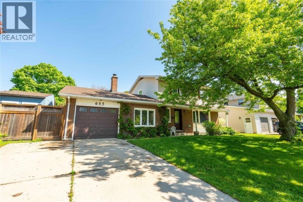 Side view of the home showing driveway and landscaping with trees - 635 Highbury Park, Sarnia