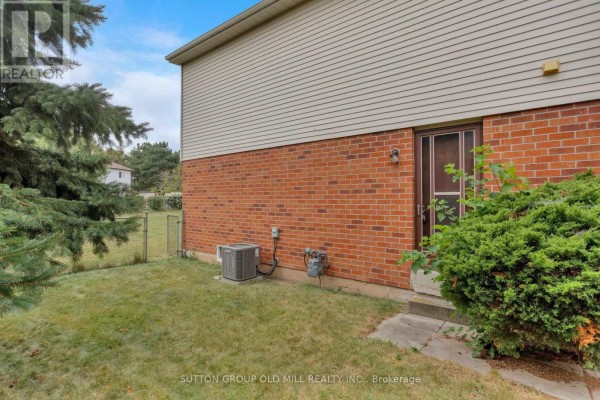 Side exterior of the house showing red brick, vinyl siding, back door, and air conditioning unit. - 6364 Plowmans Heath, Mississauga