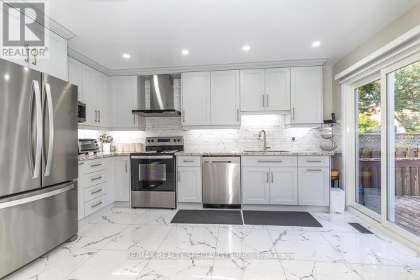 Modern kitchen with white cabinetry, stainless steel appliances, marble tile flooring, and a sliding glass door. - 6369 Longspur Road, Mississauga