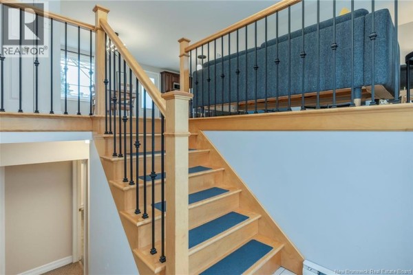 Interior view of a wooden staircase with black metal spindles and a landing overlooking a living area. - 638 Guy Avenue, Dieppe