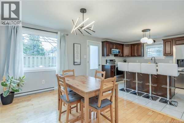 Dining area with a light wood table and chairs, adjacent to a kitchen with dark wood cabinets and island seating. - 638 Guy Avenue, Dieppe
