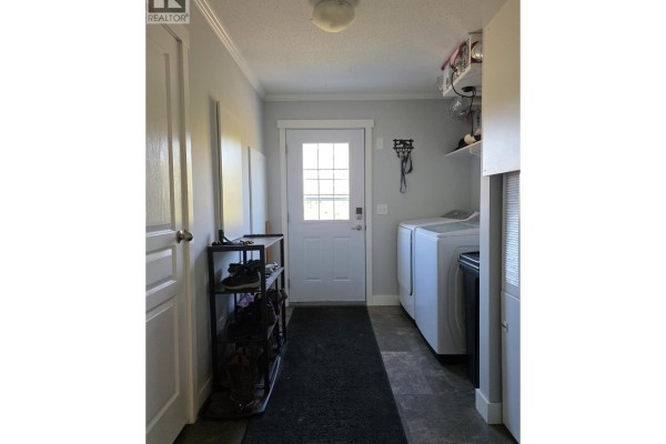 Interior view of a hallway with a washing machine, dryer, shoe rack, and a glass-paned door. - 6380 Dawsons Lane, Smithers
