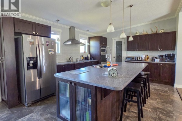 Spacious kitchen featuring dark wood cabinets, stainless steel appliances, a large island with seating, and pendant lighting. - 6380 Dawsons Lane, Smithers