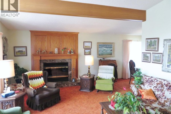 Living room with a stone and wood fireplace, orange carpet, and floral print sofa. - 639 Acadia Drive, Saskatoon