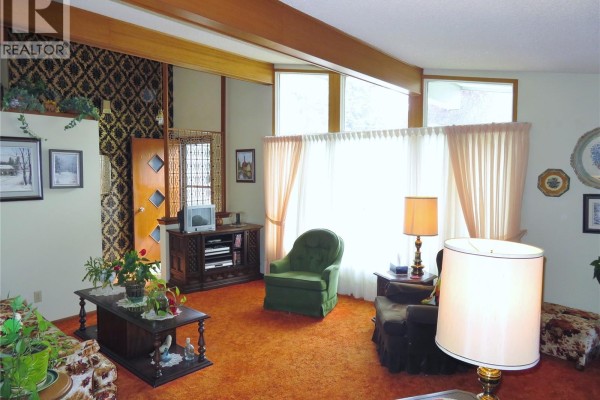 Living room with a large window, patterned wallpaper accent wall, and wood beam ceiling. - 639 Acadia Drive, Saskatoon