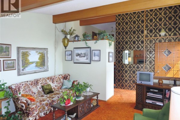 Living room showing a floral sofa, wood furniture, and decorative wall panel. - 639 Acadia Drive, Saskatoon