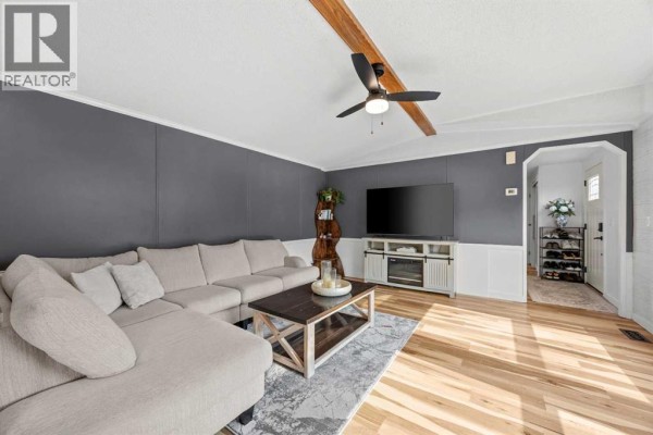 Living room with sectional sofa, television, coffee table, and hallway view to the front entrance. - 64, 1101 84 Street Ne, Calgary