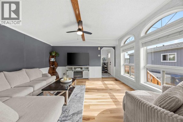 Living room with sectional sofa, television, armchair, arched windows, and hallway view to the entrance. - 64, 1101 84 Street Ne, Calgary