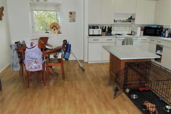Wooden dining table and chairs with children's backpacks and a kitchen area. - 64 2nd Street Se, Carman