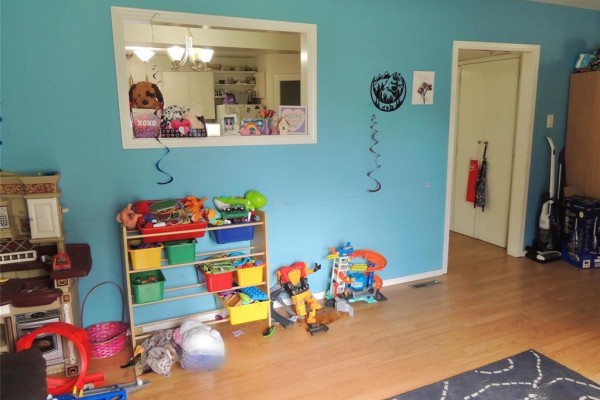 Bright blue living room with a toy shelf, play kitchen, and a doorway. - 64 2nd Street Se, Carman