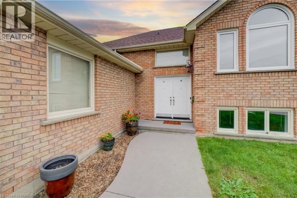 Close-up view of the brick exterior entrance with a walkway, potted plants, and double front doors. - 64 Blackfriar Lane, Brantford