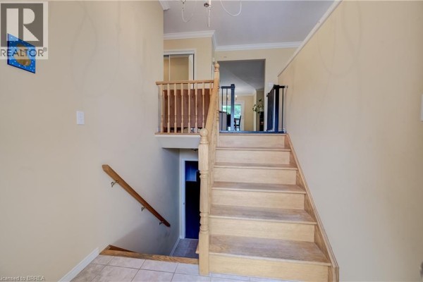 Interior view of a light beige hallway with a wooden staircase leading down to a tiled floor. - 64 Blackfriar Lane, Brantford