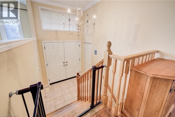 View from above the staircase looking down at the double front doors and a chandelier in the foyer. - 64 Blackfriar Lane, Brantford
