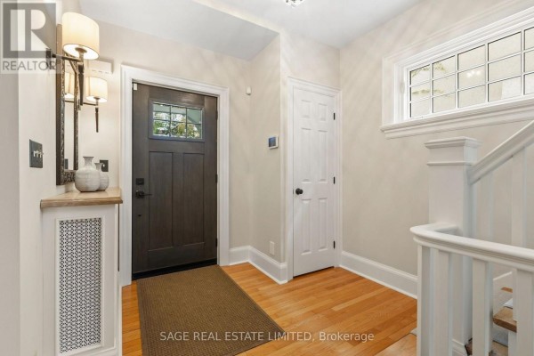 Interior entryway with dark wood front door, hardwood floors, and a white staircase. - 64 Cheritan Avenue, Toronto