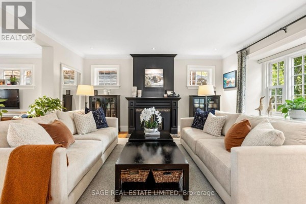 Living room with two beige sofas, a black fireplace, and large windows. - 64 Cheritan Avenue, Toronto