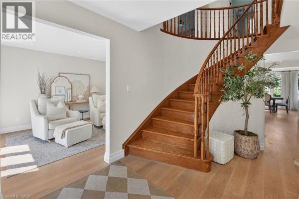 Interior foyer with a curved wooden staircase, light wood floors, and a living room view. - 64 Driftwood Court, Grimsby