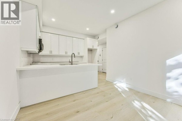Spacious white kitchen with island and view into an empty room with a door. - 64 Gage Avenue Unit# 1, Kitchener