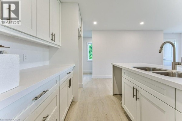 Kitchen island with sink, white cabinets, and view of living area with windows. - 64 Gage Avenue Unit# 2, Kitchener