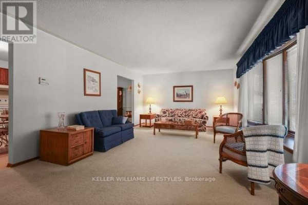 Living room with beige carpet, blue and patterned sofas, wooden furniture, and a large bay window. - 64 Haliburton Crescent, London South