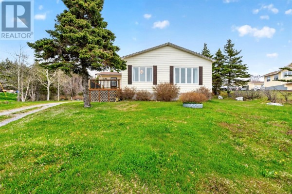 Front view of a beige bungalow with white trim and dark shutters under a blue sky. - 64 Main Road, Broad Cove  Dildo