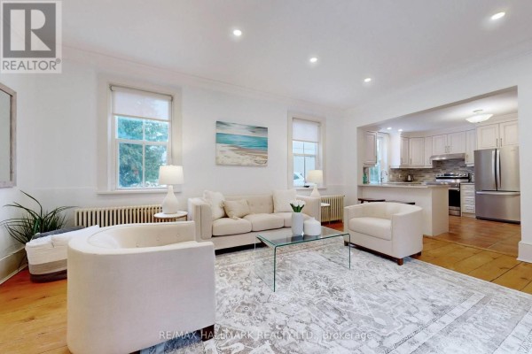 Cozy living area with two armchairs, coffee table, and visible kitchen area, neutral color scheme. - 64 Powell Street, Richmond Hill