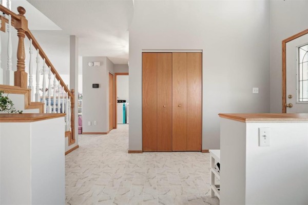 Interior hallway with wood grain closet doors, a staircase with white spindles, and a view to laundry area. - 640 Scurfield Boulevard, Winnipeg
