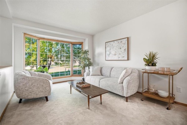 Living room with a sofa, armchair, coffee table, and large bay window with green foliage view. - 640 Scurfield Boulevard, Winnipeg