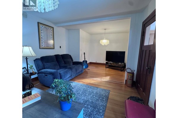Alternate view of the living room with a TV and guitar, showcasing hardwood floors. - 640 Wallinger Avenue, Kimberley