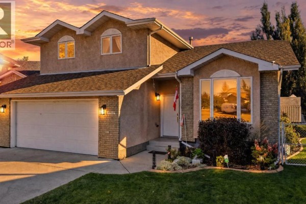 Evening view of the front of a two-story house with brick and stucco facade, double garage, and lawn. - 6404 55 Avenue, Ponoka
