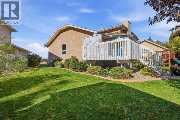 Rear exterior view of a two-story house with a stucco facade and a wooden deck, surrounded by trees. - 6404 55 Avenue, Ponoka