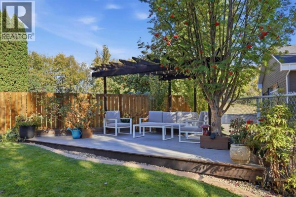 Backyard patio with white outdoor furniture under a wooden pergola, a fenced yard, and mature trees. - 6404 55 Avenue, Ponoka