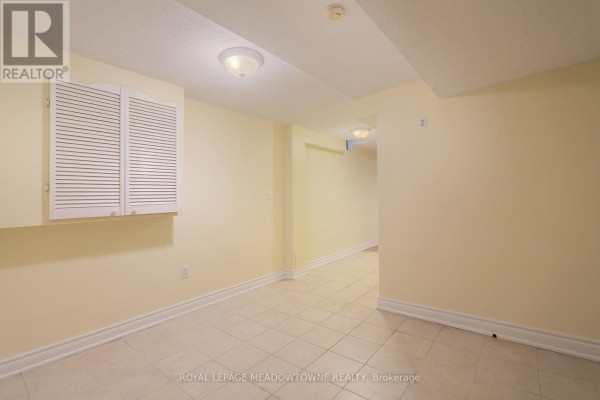 Empty room with beige walls, tiled floor, and louvered cabinet above a doorway. - 6407 Alderwood Trail, Mississauga