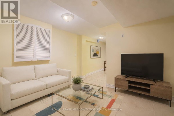 Living area with white sofa, TV on wooden stand, glass coffee table, and tiled floor. - 6407 Alderwood Trail, Mississauga