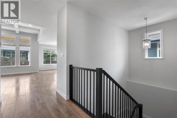 Interior hallway with wood floors, black railing staircase, and a hanging light fixture. - 641 Shuswap Road E Unit# 228, Kamloops