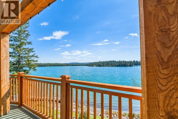 Exterior of a brown wooden house with a large deck overlooking a lake. - 6410 Fox Crescent, Green Lake