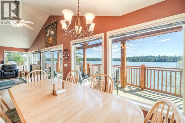 Covered wooden deck with chairs and a table, overlooking a bright blue lake. - 6410 Fox Crescent, Green Lake
