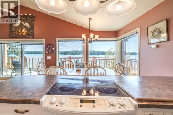 View of a house with a carport and outbuilding, set on a grassy slope by a lake. - 6410 Fox Crescent, Green Lake