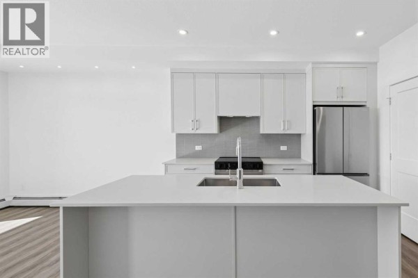 Kitchen with white island, stainless steel refrigerator, and grey tile backsplash. - 6411, 1802 Mahogany Boulevard Se, Calgary