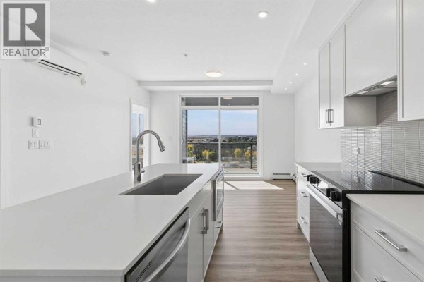 Kitchen with white cabinetry, island, stainless steel appliances, and view of houses. - 6411, 1802 Mahogany Boulevard Se, Calgary