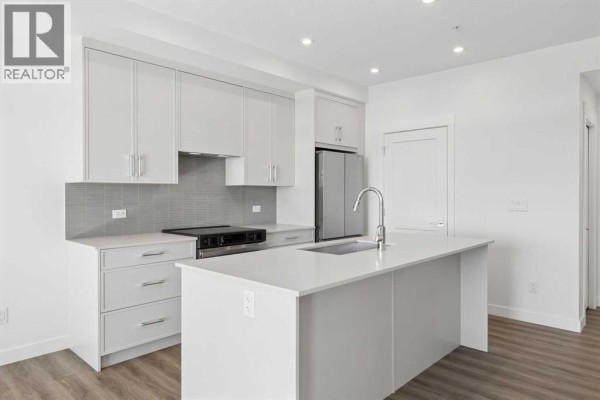 Kitchen with white island, modern grey cabinets, and stainless steel refrigerator. - 6411, 1802 Mahogany Boulevard Se, Calgary