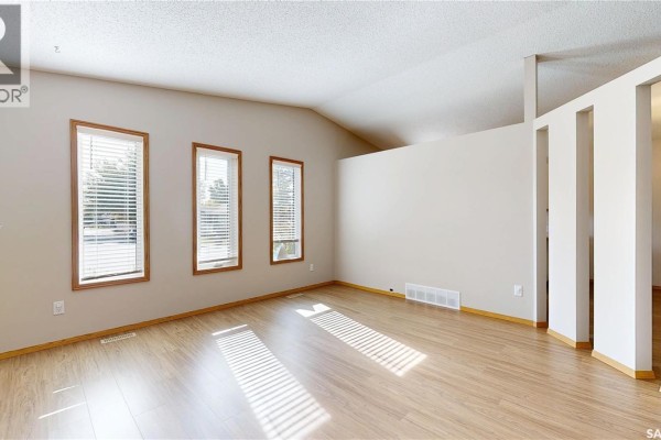 Living room with wood laminate flooring, three narrow windows on the left wall, and a vaulted ceiling. - 6418 Dalgliesh Drive, Regina