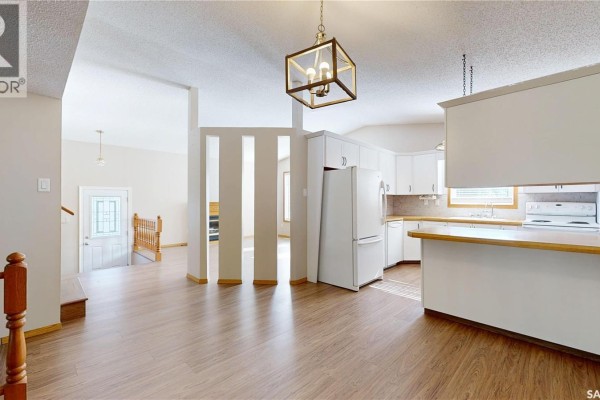 Open-concept living area showing the kitchen with white cabinets and a living room with a staircase. - 6418 Dalgliesh Drive, Regina